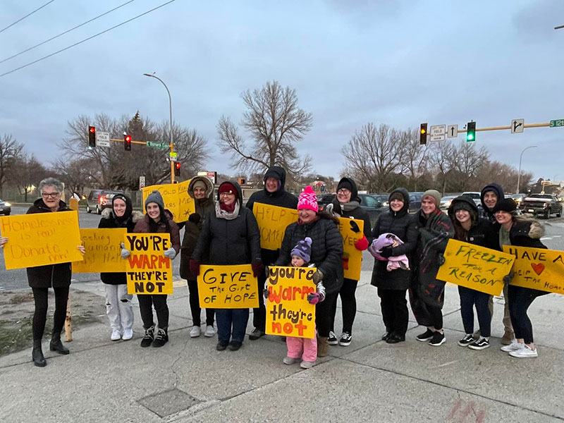 People standing outside in the cold holding signs to bring awareness to homelessness