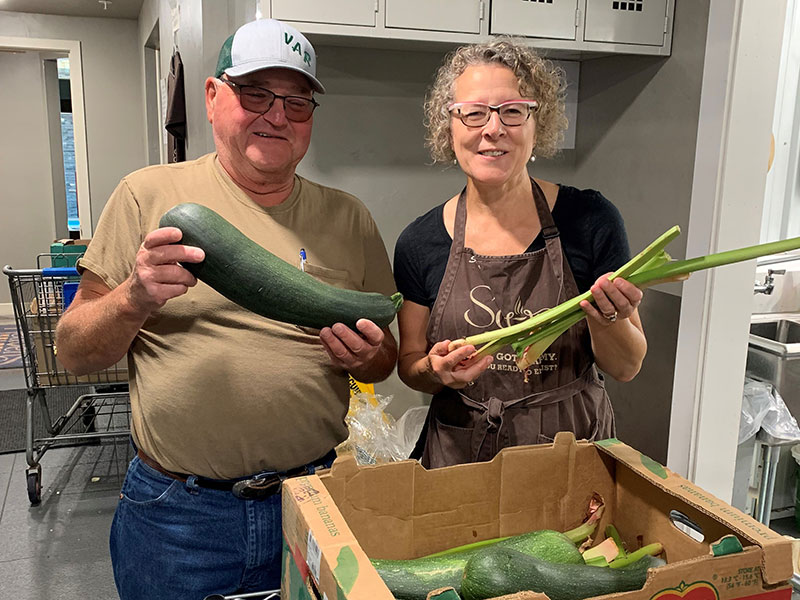 man and woman smiling and holding vegetables